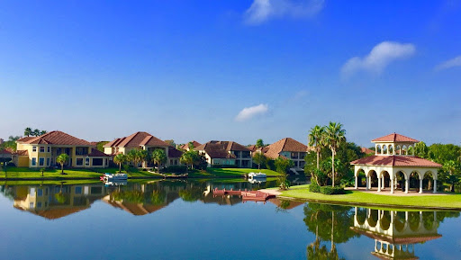 Scenic view of luxury waterfront homes in Florida with tropical landscaping, calm lake reflection, and clear blue skies, representing high-end real estate investment opportunities in Miami and Orlando.